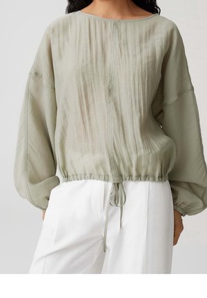 Blouse vert clair à manches longues avec ourlet froncé et lien ajustable, associée à un pantalon blanc taille haute à jambes larges.