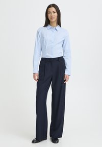 Chemise bleu clair à manches longues avec boutons, associée à un pantalon large bleu marine foncé. Tissu lisse, coupe ajustée, et col classique.