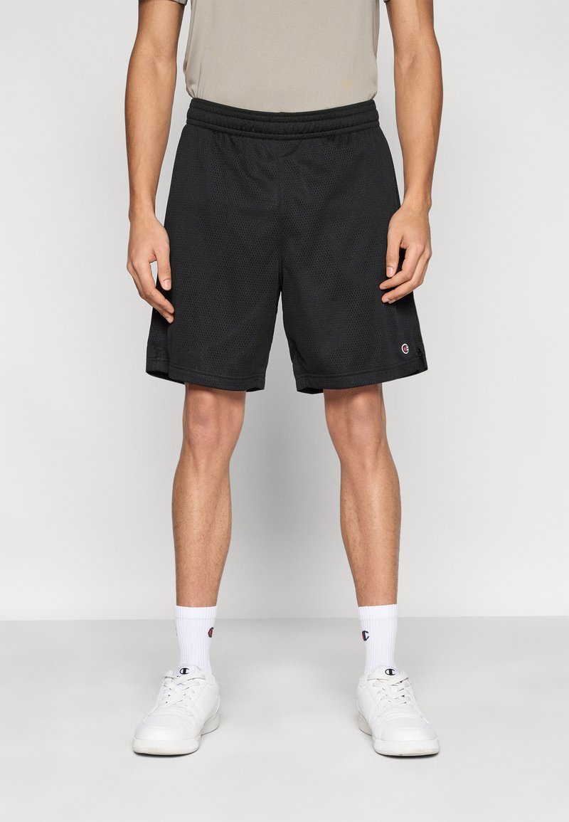 Μαύρα αθλητικά σορτς από δίχτυ με ελαστική μέση. Διαθέτουν ένα μικρό λογότυπο στη κάτω αριστερή πλευρά. Φοριούνται με λευκά αθλητικά παπούτσια και κάλτσες.