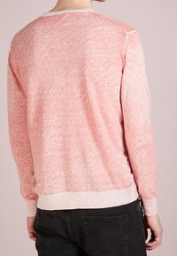 Light pink crew neck sweater with a textured finish, ribbed cuffs, and hem. Features a slightly faded appearance and contrasting neckline.