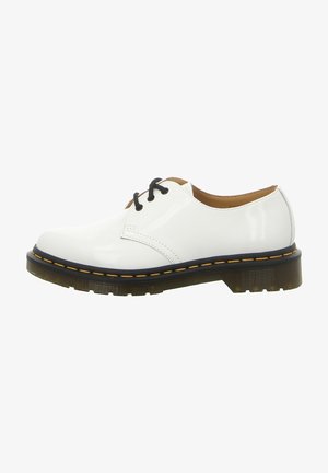Chaussure Oxford en cuir verni blanc avec lacets noirs, semelle extérieure translucide épaisse et couture jaune autour du bord de la semelle.