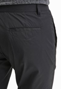 Pantalones negros con una textura suave, que presentan un bolsillo trasero único con una apertura horizontal y un sutil detalle de costura.