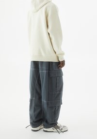 Sweatshirt surdimensionné crème et pantalons cargo amples gris foncé avec plusieurs poches et des surpiqûres contrastées, associés à des baskets blanches et grises.
