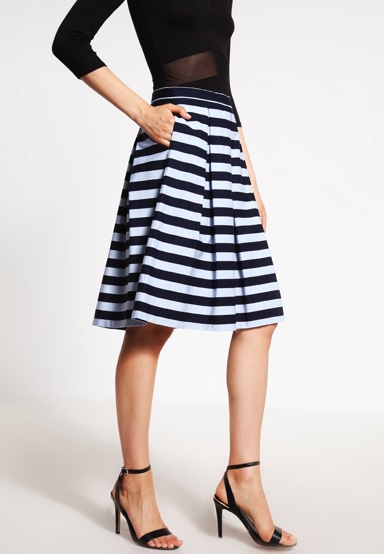 Donna con un top nero e una gonna a strisce orizzontali navy e bianche, lunga fino al ginocchio e con tasche, abbinata a sandali neri con tacco alto.