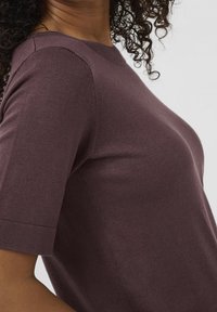 Kortærmet, tætsiddende top i mørk mauve strikket stof. Har en rund halsudskæring og glat tekstur med subtile sømdetaljer på skuldrene.