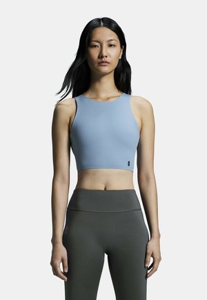 Top corto blu chiaro con scollatura arrotondata e spalline larghe, abbinato a leggings aderenti grigio scuro a vita alta. Texture liscia, design aderente.