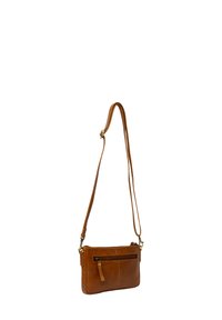 Sac en cuir brun à bandoulière réglable avec poche avant zippée, suspendu contre un fond blanc.