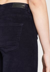 Navy corduroy broek met een textuurpatroon, achterzak en een zwart leren merklabel op de tailleband.
