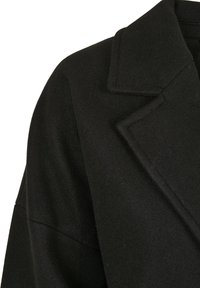 Svart ullblandingsfrakk med skrått krage, brede ermer og jevn tekstur, som fremhever minimalistisk design og rene linjer.