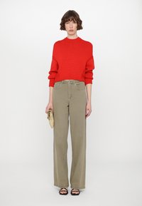 Red ribbed knit sweater with a high neck, paired with high-waisted, wide-leg olive pants. Accessories include a gold clutch and black sandals.