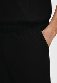 Juodos, dryžuotos sportinės kelnės su elastinga juosmena ir šonine kišene. Audinys turi tekstūrinį raštą, sukuriantį subtilų akcentą.