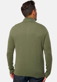 Pull en tricot vert avec un col haut, des manches longues et des poignets et un ourlet côtelés. Texture douce et design ajusté.