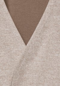 Béžový top s výstřihem do V z lehké texturované látky. Výstřih má hladkou hnědou vnitřní vrstvu, která zvýrazňuje design trička.