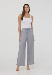 Pantaloni larghi grigi con vita regolabile, abbinati a un top bianco. Il tessuto ha una consistenza liscia e una leggera lucentezza.