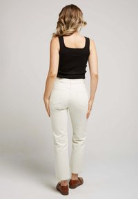 Top sans manches noir avec des bords en dents de scie, associé à un pantalon droit de couleur crème et des chaussures marron, vu de dos.