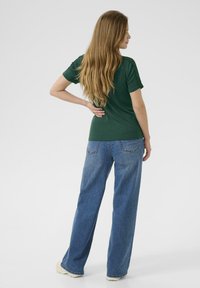Haut vert à manches courtes avec épaules texturées associé à un jean large bleu clair. La tenue présente une coupe décontractée et un style casual.