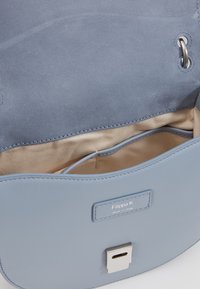 Sac à main en cuir bleu clair avec une texture lisse, équipé d'un fermoir en métal argenté et d'une doublure intérieure beige avec une poche supplémentaire.