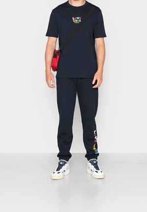 Mörkblå bomullst-shirt med texten "LOVE WINS" i regnbågens färger, kombinerad med mörkblå mjukisbyxor. Vita sneakers med svarta detaljer och gröna inslag.