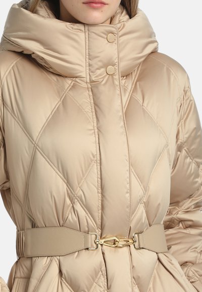 Beige vatteret jakke med høj krave, der har en cirkulær knaplukning og en bælte-liv med en spændeaccent i guldtonet.