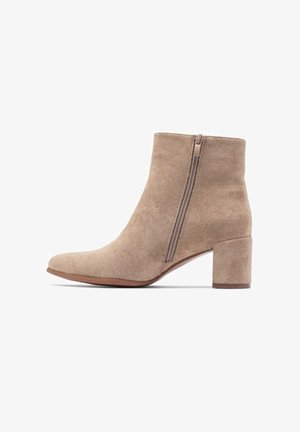 Beige Wildleder-Stiefelette mit seitlichem Reißverschluss und niedrigem klobigem Absatz, von der Außenseite auf weißem Hintergrund gezeigt.