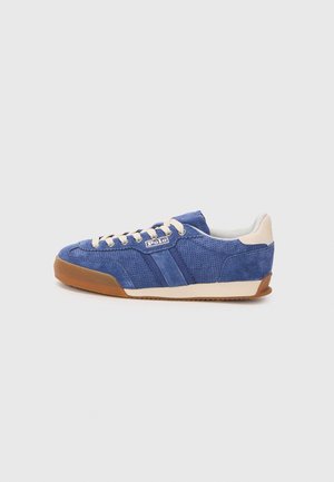 Niebieski zamszowy sneaker z beżowymi sznurowadłami, brązową gumową podeszwą, bocznym logo "Polo" i białym wyściełanym kołnierzem przy pięcie na szarym tle.