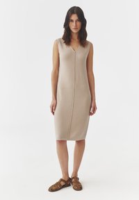 Triko, bezramenn dresses ve světle béžové barvě s výstřihem do V a detailem předního švu, sahající po polovinu lýtek. Kombinováno s hnědými sandály na řemínky.