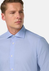 Gaiši zils svītrainais krekliņš ar asu apkakli, pogām priekšpusē un vieglu faktūru. Iezīmējas ar baltām pogām un piegriezumu, kas pielāgots ķermenim.