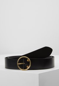 Ceinture en cuir noir avec une boucle en or circulaire. La ceinture présente une finition texturée et une extrémité effilée lisse.