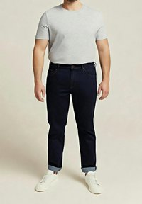 Camiseta gris de manga corta, vaqueros azul oscuro con los puños remangados y zapatillas blancas. Atuendo casual, con un diseño sencillo y limpio.