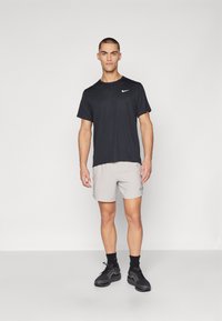 Black short-sleeve t-shirt with Nike logo, paired with light gray shorts and black athletic shoes, featuring textured fabric and elastic waistband.