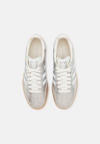 Silver sneakers with white stripes, round toe, textured upper, and beige rubber sole; features white laces and branding on the tongue.