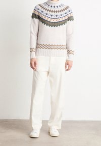 Sweter robiony na drutach w jasnoszarym kolorze z wzorzystą ramionką w niebieskie, zielone i pomarańczowe diamenty, w połączeniu z białymi spodniami o szerokich nogawkach oraz trampkami.