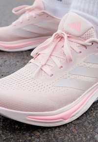 Rosa treningssko med mesh-overdel, kontrasterende hvite striper og en teksturert gummisåle med en fremtredende rosa aksent.