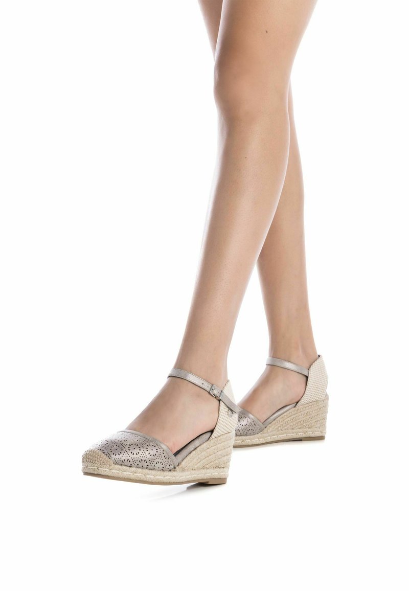 Alpargatas cuña en beige metálico con detalles troquelados, suela de yute tejido en beige y correa ajustable en el tobillo.