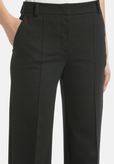 Zwarte op maat gemaakte broek met een gladde textuur, voorzien van zijzakken, scherpe plooien en een recht gesneden ontwerp. Verminderde bulk bij de taille.