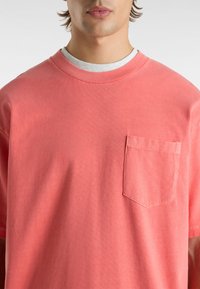 Koralfarbenes Baumwoll-T-Shirt mit Rundhalsausschnitt, kurzen Ärmeln und einer Brusttasche. Der Stoff hat eine glatte Textur und dezente Nähdetails.