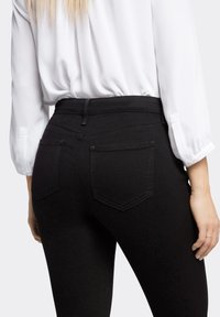 Hofteskårne sorte jeans med en glat tekstur, forstærket syning og to baglommer, stylet med en hvid bluse.