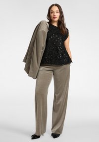Czarny top z cekinami o kwiatowej fakturze, zestawiony z miękkimi szerokimi spodniami z aksamitu w kolorze taupe oraz dopasowaną marynarką, uzupełnione czarnymi butami na obcasie.