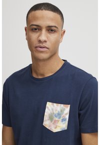 T-shirt in cotone blu navy con taschino anteriore decorato con un motivo tie-dye multicolore. Maniche corte e scollatura rotonda.