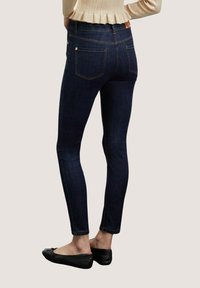 Jeans ajustados de denin oscuro, con una textura suave, diseño clásico de cinco bolsillos y detalles de costura sutiles. Combinados con zapatos planos negros.