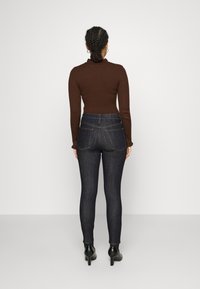Vaqueros de mezclilla ajustados de color azul oscuro con cintura alta, combinados con una camiseta de manga larga de canalé marrón. Presentan bolsillos traseros y un diseño elegante.