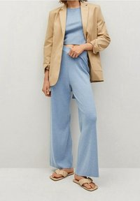 El conjunto incluye un blazer ajustado beige, una blusa corta azul claro y pantalones anchos azules, acompañados de unas chanclas marrones con tiras rizadas.