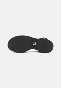 Black shoe sole with a smooth finish, contoured shape, circular metallic accent, and subtle textured grip pattern.