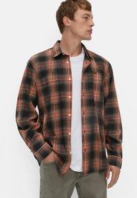 Rød og sort plaid flannel skjorte med knap-ned krave, lange ærmer, brystlomme og hvid undertrøje, parret med grå bukser.