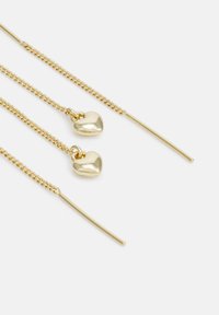 Boucles d'oreilles en métal doré avec deux pendentifs en forme de cœur et de fines chaînes, présentant une finition polie et des accents en bâton allongés.