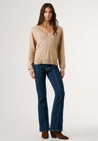 Bež pulover sličnog v-izreza, dugi rukavi, rebrast završetak; uparen s tamnoplavim razgužvanim farmerkama i smešnim čizmama do gležnja. Glatka tekstura, ležište dizajn.