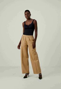 Juoda be rankovių palaidinė su priekinėmis skylutėmis, derinama su šviesiai rudos spalvos plačiakelnėmis kelnėmis ir juodais aukštakulniais bateliais su akcentais.