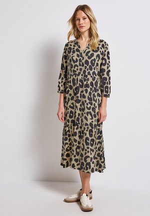 Robe à imprimé léopard, à manches longues, à volants en vert olive et noir, dotée d'un décolleté en V et d'une coupe décontractée, associée à des baskets blanches.