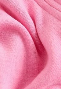 Un tissu tricoté rose clair présentant une surface douce et texturée avec des coutures fines. Le matériau semble flexible et tombe en douceur.