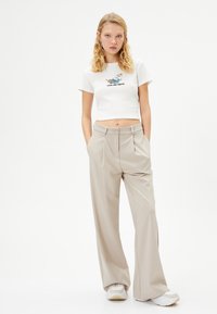Top court côtelé blanc avec un graphique de chat et le texte "LES CHATS SONT LIQUIDES" ; pantalon large taille haute beige ; baskets claires.